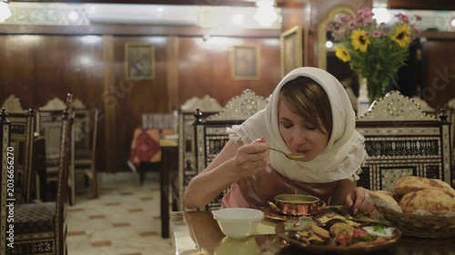Slow motion shot of female traveler tasting traditional soup at authentic restaurant in Cairo, Egypt. Woman in headscarf enjoying local Middle Eastern cuisine in warm oriental atmosphere captured in c