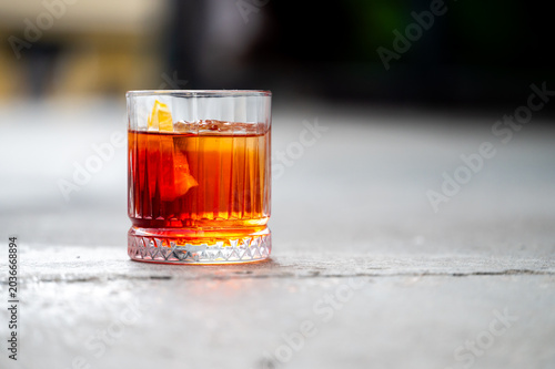 Fotografi A classic Negroni cocktail with an orange peel garnish is served in a crystal rocks glass on a rustic concrete surface, close-up shot with a shallow depth of field