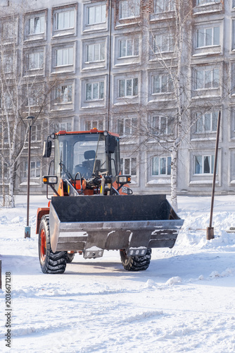 Fotografía Snow removal tractor operates in a residential area, clearing snow from the grou