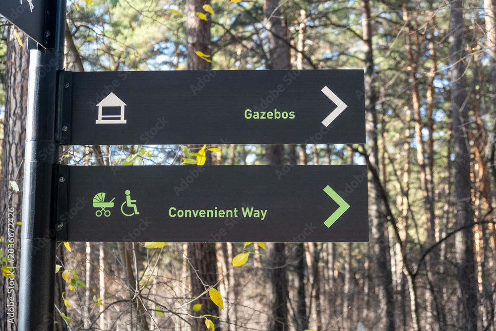Obraz premium Directional signpost displays arrows for gazebos and convenient way, surrounded by trees and natural foliage in a wooded area