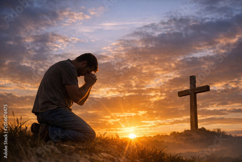 A man kneeling down and praying with a cross in the background at sunset. The sky is filled with clouds, creating an atmospheric scene.