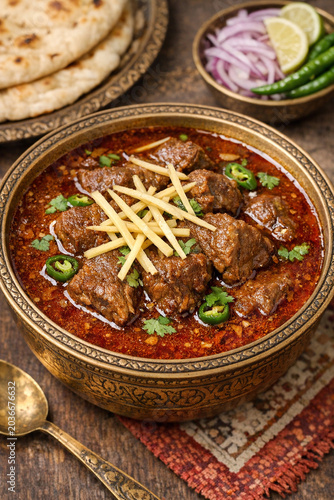 A bowl of beef curry soup garnished with toasted bread on a table. The soup is served with naan bread and lime wedges for added flavor.