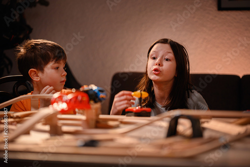 Playful sister making train sounds while brother watches during wooden railway playtime at home