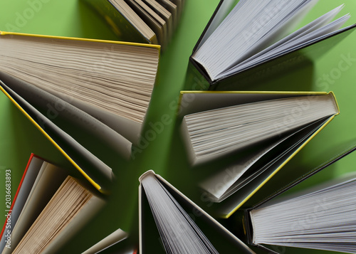 Top view of open books arranged on green background. Minimal educational composition with stacked books and copy space. Reading, learning and knowledge concept with clean flat lay style.
