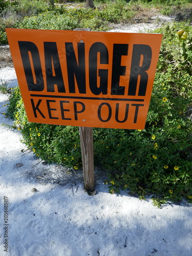 Danger keep out sign posted in beach white sand with plants vertical photo