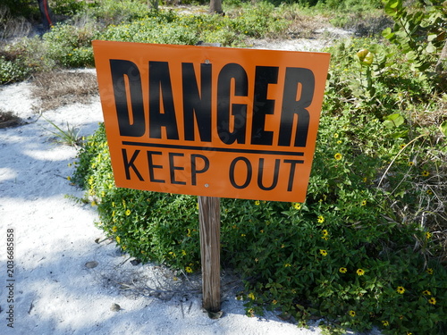 Danger keep out sign posted in beach white sand with plants