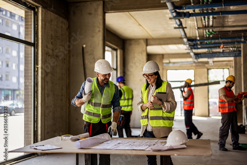фотографія Male and female architects reviewing renovation blueprints with builders working in the background