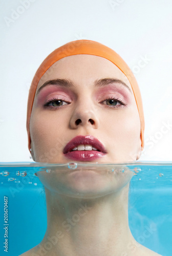 Portrait of beautiful young woman in swim cap looking at camera in swimming pool.