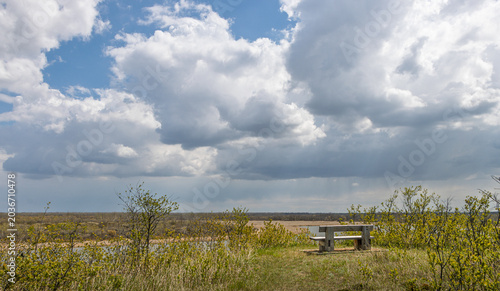 Tableau sur toile There is a summer storm brewing in the sky and thick clouds are floating over a lake towards an empty wooden bench