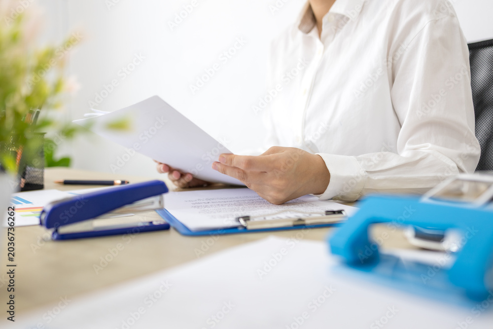 Fototapeta premium Woman smiles while holding a blank document at her desk. Office supplies lie scattered around her workstation. Her expression shows calm focus and satisfaction 