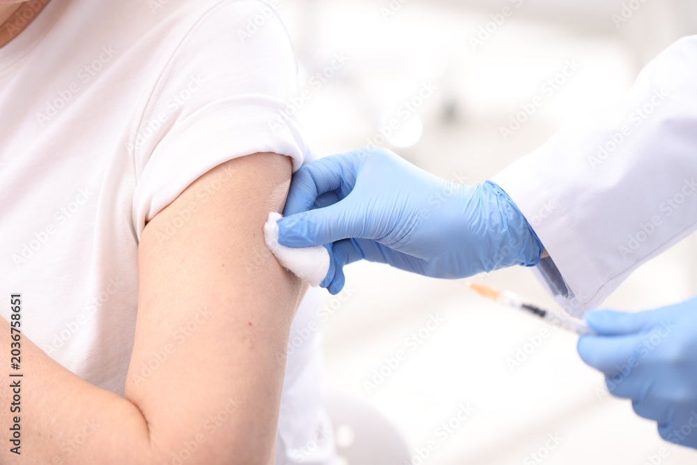 Fototapeta premium Doctor in medical gloves pressing patient's injection site after vaccination with cotton wool against blurred background, closeup