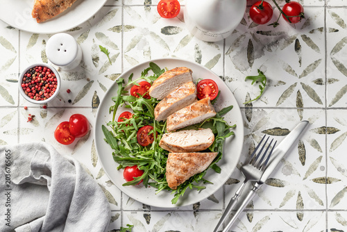 Grilled chicken breast and green vegetable salad on white plate, healthy food on printed tile background top view