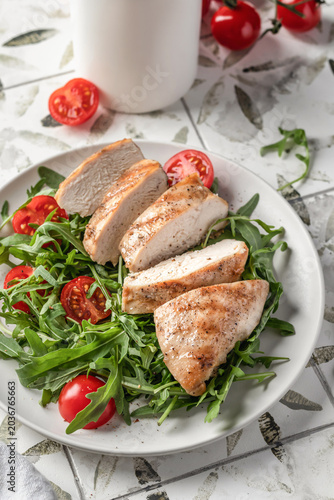 Grilled chicken breast and green vegetable salad on white plate close up, healthy food on printed tile background