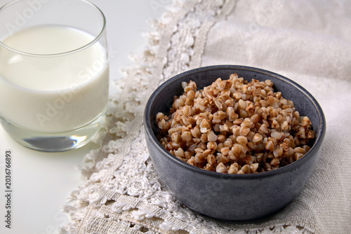 Tableau sur toile Cooked buckwheat groats in a ceramic bowl and a glass of milk on a linen tablecl