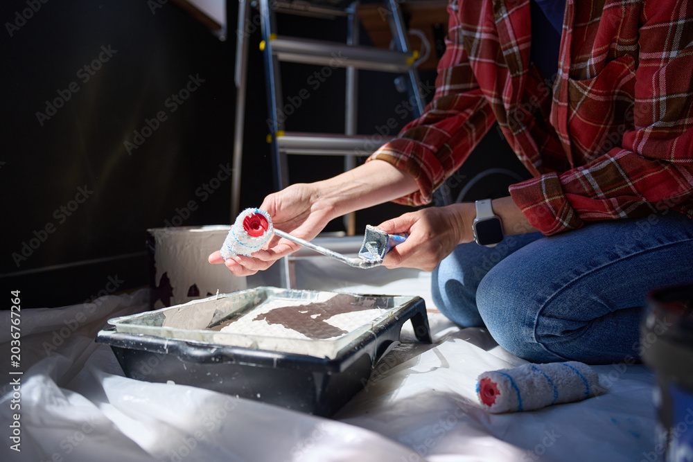 Fototapeta premium Person attaches paint roller cover over tray beside paint bucket on plastic sheet