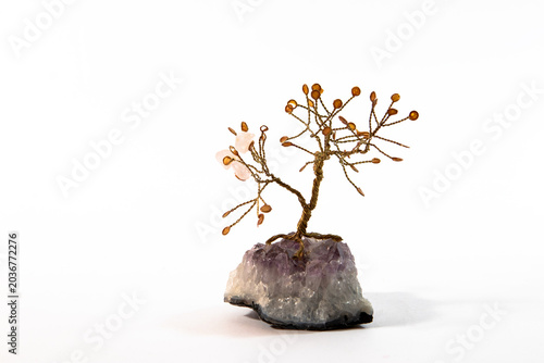 A handmade wire gemstone tree with pink quartz crystal leaves growing from an amethyst crystal cluster base isolated on a clean white background