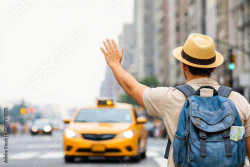 Male tourist with backpack waving hand to hail a yellow taxi on city street
