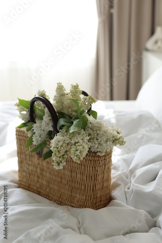 White lilac flowers in wicker basket on bed indoors