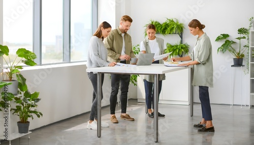 Equipo de profesionales trabajando de pie en una mesa alta con portátil en oficina moderna y luminosa