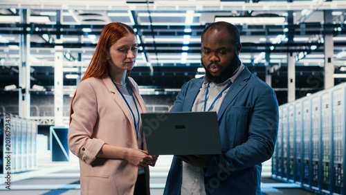 Quadro su tela Server farm manager teaching intern to use laptop and optimize electronics during induction, Data center team leader and trainee using notebook to monitor system performance, camera B