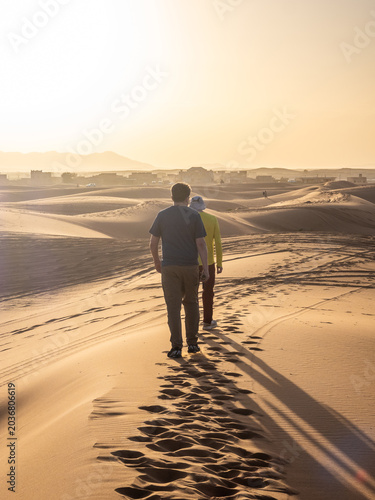 Travelers walking across golden Sahara dunes at sunset near Merzouga, Morocco