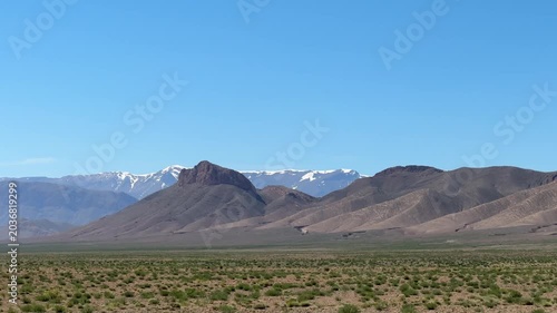 Snow-capped Atlas Mountains rising above arid Moroccan landscape under blue sky