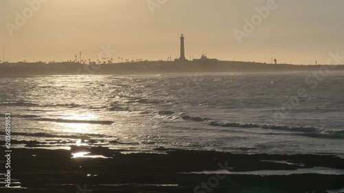 Atlantic coastline at sunset with lighthouse silhouette and ocean waves in Casablanca