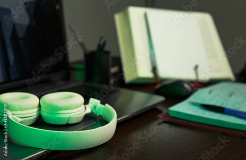 An education, school desk with a laptop, an open book, white headphones, colorful pens for art or study supplies. No people, nobody. A detail of the workspace on a wooden table. Different angles