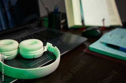 An education, school desk with a laptop, an open book, white headphones, colorful pens for art or study supplies. No people, nobody. A detail of the workspace on a wooden table. Different angles