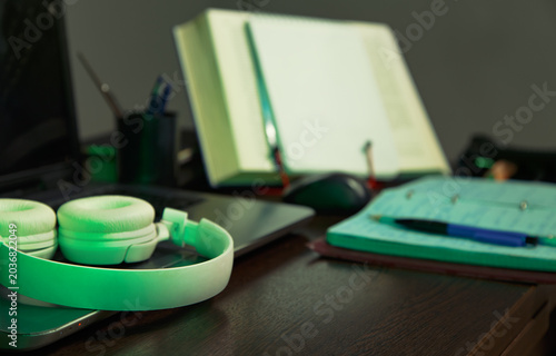 An education, school desk with a laptop, an open book, white headphones, colorful pens for art or study supplies. No people, nobody. A detail of the workspace on a wooden table. Different angles