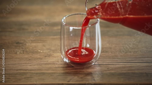 Close-up of fresh tomato juice being poured into a clear glass, highlighting its rich red color and smooth liquid texture. The image represents healthy eating, natural ingredients, and hydration.