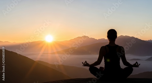 Woman practicing yoga on mountain summit during beautiful sunrise.
