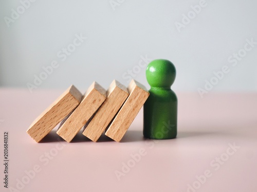 Photos Minimalist studio shot of a green wooden pawn preventing a stack of wooden blocks from collapsing over a soft pinkish surface