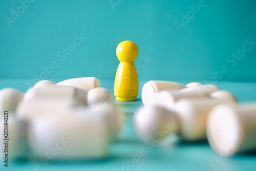 Fotografie Low-angle, selective-focus shot of a yellow wooden peg doll standing amidst a background of fallen white figures, conceptualizing resilience, stability, or surviving a layoff