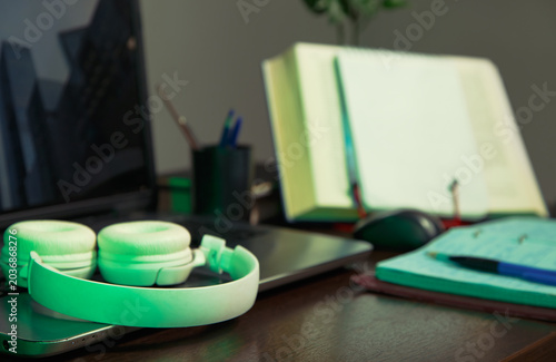 An education, school desk with a laptop, an open book, white headphones, colorful pens for art or study supplies. No people, nobody. A detail of the workspace on a wooden table. Different angles