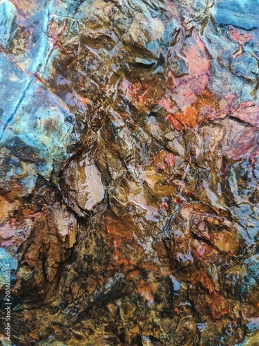 Rugged wet gold-bearing ore showcasing sharp fractured stone layers with striking pale blue mineral tones and deep amber-iron oxide staining