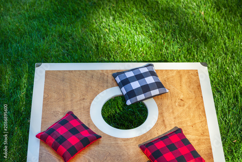 Overhead view of a corn hole board on grass with plaid bean bags on it