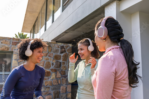 Quadro su tela Diverse female friends laughing and chatting on patio by stone wall wearing gym