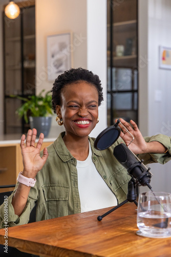 African American woman smiling and speaking into mic while recording in home studio at wooden table