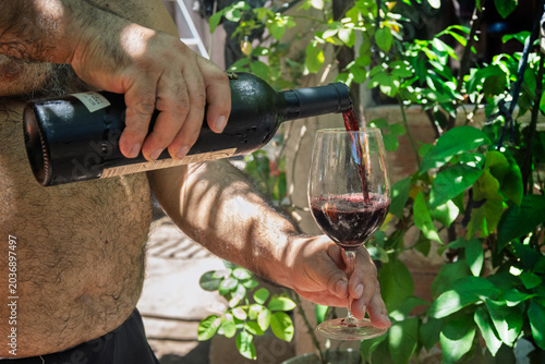 Sirviendo copa de vino tinto argentino en previo al asado familiar al aire libre, tradición social y cultural típica