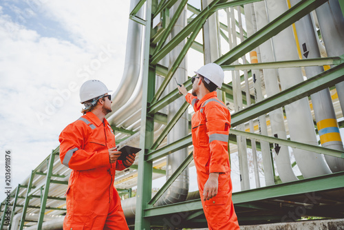 Engineers in gas and oil industry inspecting pipeline structure at refinery using digital tablet