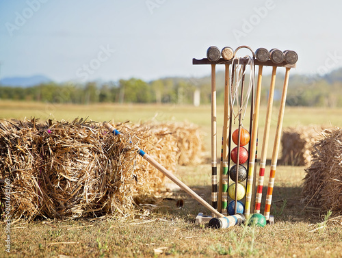 Obraz na plátně Colorful croquet equipment arranged beside hay bales on a sunny rural field, capturing a relaxed outdoor lawn game atmosphere with vintage sporting charm