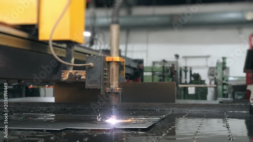 Industrial CNC plasma cutting machine processing metal sheet with sparks in factory. Automated metal fabrication and manufacturing technology.