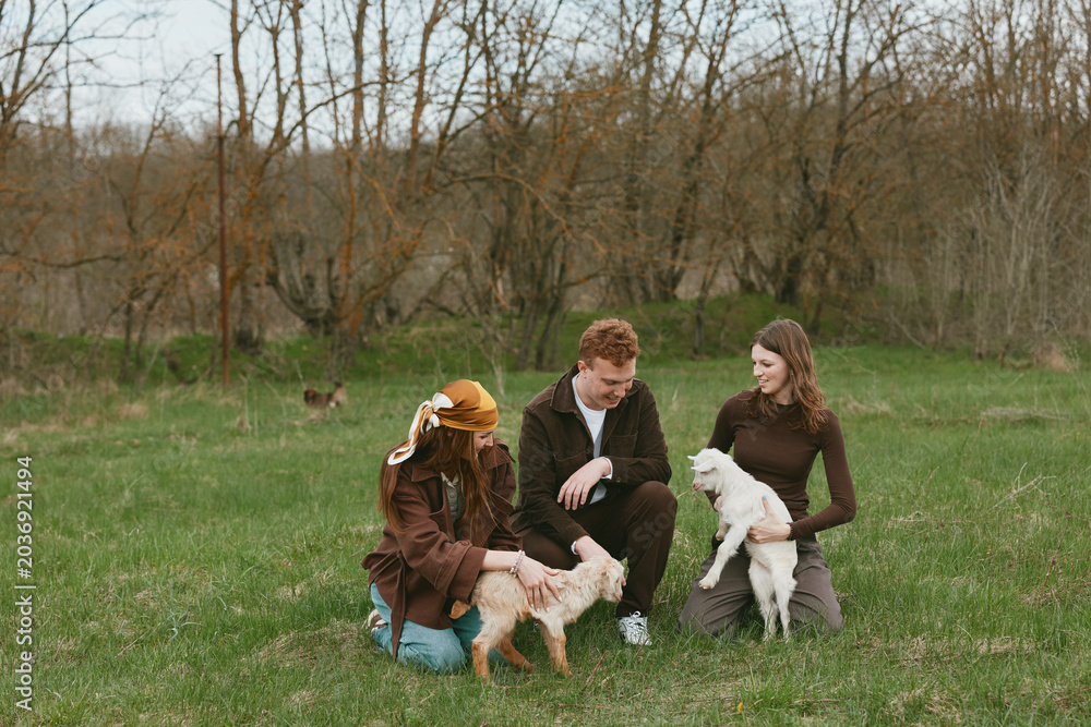 Fototapeta premium Goat kid lifestyle outdoor scene with friends in a park, featuring a friendly animal and pet companionship, as nature sunlight and smiles capture joyful interaction and warm togetherness.