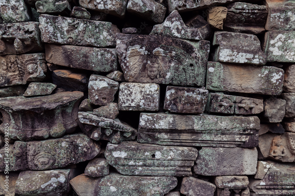 Fototapeta premium Ancient stone carvings of figures and mythical creatures adorn the weathered walls of Bayon Temple, Angkor Wat, Siem Reap, Cambodia, showcasing intricate Khmer artistry.