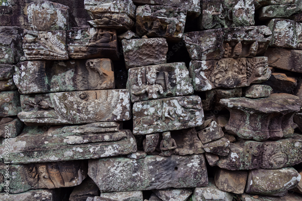 Fototapeta premium Ancient stone carvings of figures and mythical creatures adorn the weathered walls of Bayon Temple, Angkor Wat, Siem Reap, Cambodia, showcasing intricate Khmer artistry.