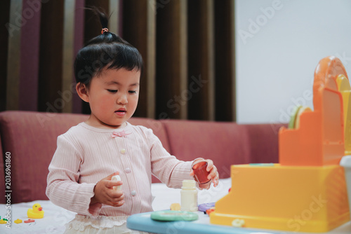 Photos Medium shot of a cute little Asian girl with a top knot hairstyle playing with k