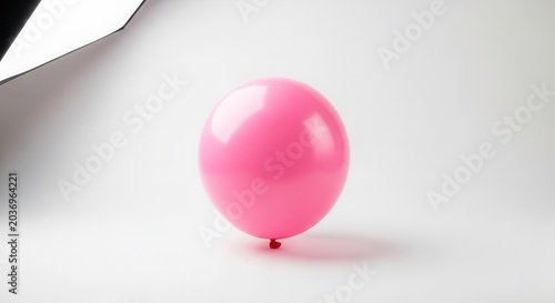 A single pink balloon floats against a bright white background with studio lighting.