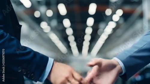 Businessman and engineer shake hands in car factory, close up. Buyer of car shaking hands with seller in auto dealership. Concept of choosing and buying new car at showroom.
