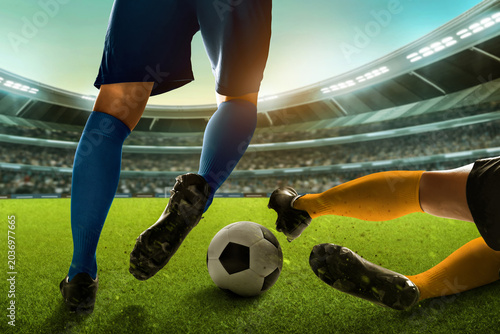 Two professional soccer player legs, blue sock dribbling ball and yellow sock sliding tackle in the stadium field